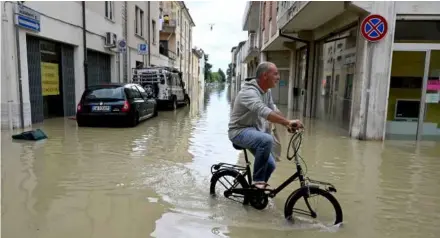  ?? AFP/VNA Photo ?? A man rides in a flooded street in the town of Lugo on May 18, after heavy rains caused flooding across Italy's northern Emilia Romagna region. Rescue workers searched on May 18 for people still trapped by floodwater­s in northeast Italy as more residents were evacuated after downpours which killed nine people and devastated homes and farms.