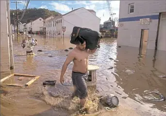  ?? Steve Mellon/Post-Gazette ?? A man carries luggage filled with belongings from his home on flooded Cherry Street in Etna in 2004, after remnants of Hurricane Ivan flooded the street the day before.