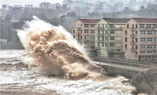  ??  ?? WAVES hit a sea wall in front of buildings in Taizhou, China’s eastern Zhejiang province.