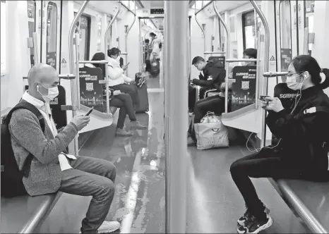  ?? WANG JING / CHINA DAILY ?? Passengers wearing earphones use their mobile phones during a subway trip in Wuhan, capital of Central China’s Hubei province, on March 29.