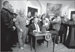  ?? DOUG MILLS / THE NEW YORK TIMES ?? President Donald Trump, joined by steel workers, hands out the pens March 8 after signing an order imposing sweeping new tariffs on imported steel and aluminum at the White House.