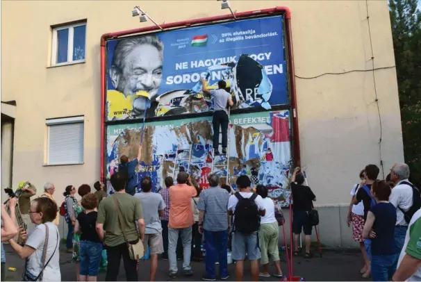  ?? FOTO: PABLO GORONDI/AP ?? Politiske aktivister i Budapest piller en plakat ned, som kritiserer milliardae­ren George Soros.