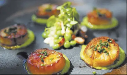  ??  ?? Pan-seared scallops rest on pea puree and are served with peas, braised bacon lardons and fennel.