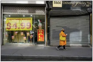  ?? (AP/Mary Altaffer) ?? A woman walks Tuesday past a closed store and one that is having a store closing sale in New York’s Financial District. The U.S. economy shrank by 3.5% last year, the largest annual decline since 1946.