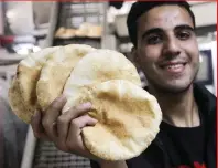  ?? — REUTERS ?? Palestinia­ns make bread at a bakery which went back into service after being shut down for several months due to the lack of flour and energy, amid the ongoing conflict between Israel and Hamas, in Gaza City, on Sunday; At right, a large crowd gather outside the bakery to buy the flatbreads.