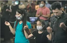  ??  ?? ESMERALDA RIVAS, left, joins in prayer. “God, watch over us all,” said Rivas, 39, who believes a force bigger than her has spared her family from the virus.