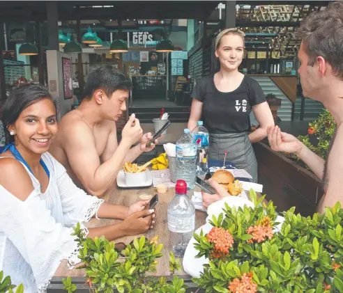  ?? Picture: ANNA ROGERS ?? TRAVEL CONNECTION­S: English tourists Manini Bharadwaj, Tim Chau and Stewart Smith are served by Courtney Rodd during lunch at Grill'd on the Cairns Esplanade.