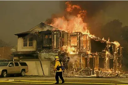  ?? —AP ?? Afireman walks near a flaming house in Santa Rosa as the California wildfire continued to consume everything in its path, leaving nothing but posts (top photo) in this house also in Santa Rosa.