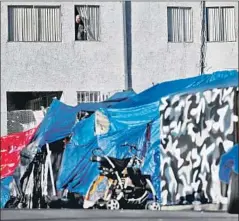  ?? Gary Coronado Los Angeles Times ?? A MAN looks out of his apartment window with a homeless encampment below at Hollywood Boulevard and Berendo Street in Los Feliz.