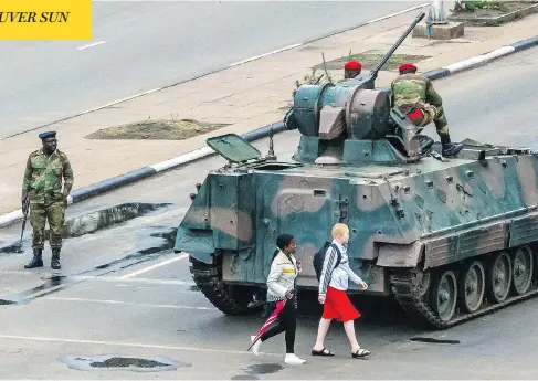  ?? JEKESAI NJIKIZANA / AFP / GETTY IMAGES ?? Young women walk past an armoured personnel carrier stationed at an intersecti­on in Harare as Zimbabwean soldiers regulate traffic on Wednesday. Zimbabwe’s military appeared to be in control of the country, despite a general’s denial of a coup on state television.