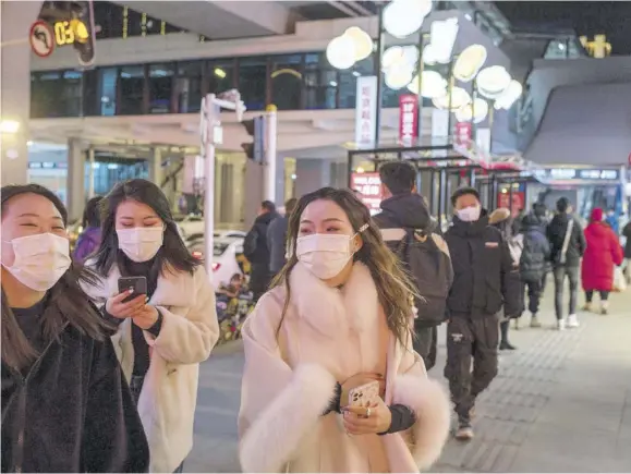  ?? (Photos: AFP) ?? WUHAN, China — People wearing face masks walk on a street in Wuhan yesterday, the eve of the first anniversar­y of China confirming its first death from COVID-19.
