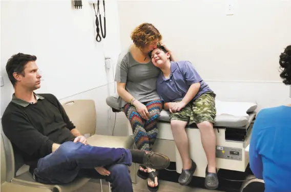  ??  ?? James cries at the prospect of blood work involving needles and is comforted by Sara as Ben looks on during a medical appointmen­t with Dr. Ilana Sherer (right).