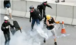  ?? —AFP ?? A protester (R, in yellow helmet) swings a tennis racquet to return a tear gas canister fired by riot police at Kowloon Bay in Hong Kong on Saturday, August 24