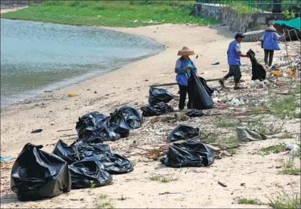  ?? BOBBY YIP / REUTERS ?? Workers clean up trash washed ashore on Nim Shue Wan beach, Lantau Island, Hong Kong. Researcher­s say the waters off the city face challenges from pollution from many sources, including discarded waste and chemical pollutants.