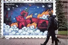  ?? Efrem Lukatsky/Associated Press ?? Residents of Kyiv pass an image of a new postage stamp design that depicts a fire burning through the Kremlin in Moscow.