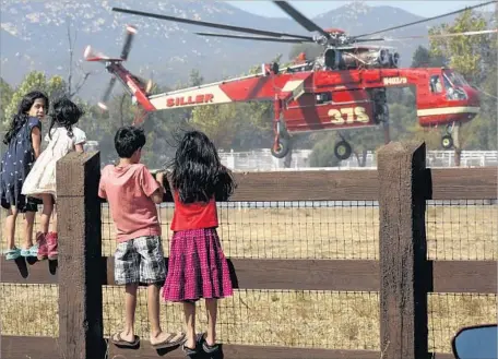  ?? Irfan Khan Los Angeles Times ?? CHILDREN WATCH as an air crew loads water to battle the Wildomar fire. Firefighte­rs had the blaze 50% contained by Friday evening.