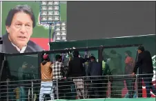  ?? — AFP photo ?? Workers install a bullet proof glass shield on the main stage of the venue ahead of an anti-government rally led by Imran Khan (shown on poster) in Rawalpindi.