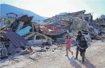  ?? YASIN AKGUL/AFP VIA GETTY IMAGES ?? People on Sunday walk by the rubble of the historic southern city of Antakya, Turkey.