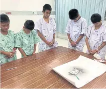  ??  ?? The ‘Wild Boars’ footballer­s and their coach stand in silence and write a message of condolence on the painting of former Navy Seal LCdr Saman Gunan after learning of his death during the operation to rescue them from the flooded Tham Luang cave complex.