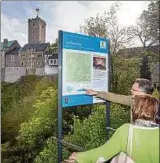  ??  ?? Wanderer betrachten vor der Wartburg in Eisenach ein Hinweissch­ild zum Lutherweg. Foto: M. Reichel,dpa