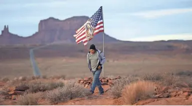  ?? PHOTOS BY RICK BOWMER/AP ?? Brandon Nez displays his flag near his jewelry stand in Monument Valley, Utah, where tourists stand in the highway to recreate a famous running scene from the movie “Forest Gump.”