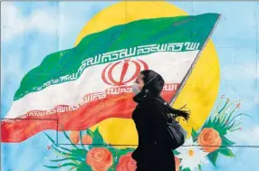  ??  ?? Una mujer camina frente a un mural nacionalis­ta con la bandera nacional iraní, en calles de Teherán, Irán