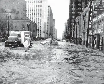  ?? Bill Knight Los Angeles Times ?? A MORNING STORM dumped 2.32 inches of rain before noon on Feb. 19, 1958, forcing these stranded drivers to wade toward the sidewalks on Flower Street between 5th and 6th streets in downtown Los Angeles.