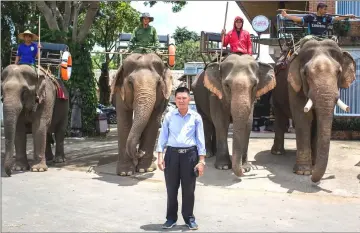  ??  ?? Dang Nang Long, owner of an elephant trekking tour company, posing in front of his elephants at a tourist resort in Lien Son town.