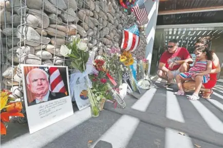  ?? Ralph Freso, Getty Images ?? A family kneels down and places flowers at a small memorial to pay their respects to the late Sen. John McCain on Sunday outside his office in Phoenix.