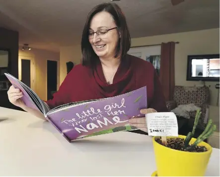  ?? ED KAISER ?? Cynthia Strawson looks at a children’s book given to her by the Fort McMurray family that stayed in her Edmonton home during the wildfire crisis. The potted plant also was a gift from Isabel, who was seven when her family briefly lived on the main floor of Strawson’s home while Strawson lived in the basement.