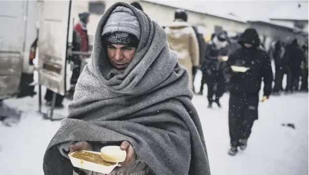  ?? PICTURE: ANDREJ ISAKOVIC/AFP/GETTY IMAGES ?? 0 A migrant receives a hot meal from volunteers outside derelict warehouses which they use as a makeshift shelter, in Belgrade as temperatur­es dropped to -15C overnight. According to the latest figures, around 7,000 migrants are stranded in Serbia