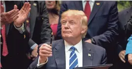  ?? ANDREW HARNIK/AP ?? President Donald Trump holds a pen he used to sign one of various bills in the Roosevelt Room of the White House on Monday in Washington.
