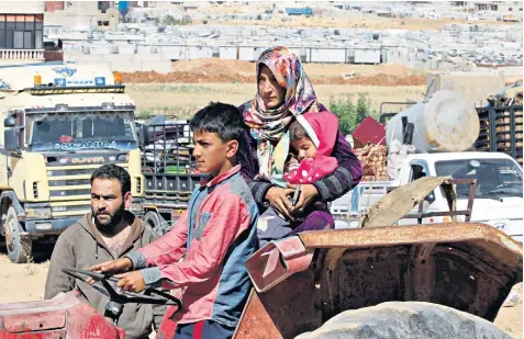  ??  ?? A Syrian family in the Lebanese border town of Arsal prepares to cross back into their country earlier this summer. Below, returning refugee Khola Betjen with her child last week