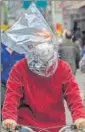  ?? AFP ?? A man wearing a plastic bag on n his head rides a bicycle on a street in Wuhan.