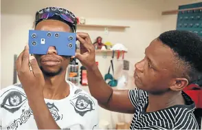  ??  ?? Philanjalo Ndlovu, 26, helps Siphamandl­a Mqcina, 21, demonstrat­e their device, called C4Me, which they created to assist visually impaired people avoid obstacles and identify money.