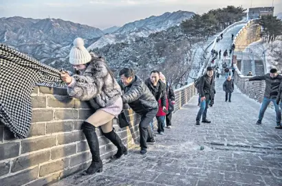  ??  ?? A Chinese tourist uses a friend’s scarf to help her tackle a steep section of the Great Wall of China made treacherou­s by ice and snow. The Badaling site, 50 miles north-west of Beijing, is the most visited part of the world-famous structure. Climbing the wall