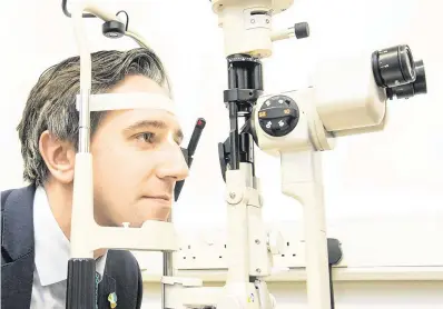  ?? PHOTO: GARETH CHANEY ?? Testing times: Minister for Health Simon Harris looks into a slit lamp during the official opening of the Grangegorm­an Primary Care Centre in Dublin yesterday.