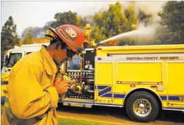  ??  ?? A Ventura County firefighte­r makes a call over his radio as colleagues work Friday to contain a wildfire along Lindero Canyon Road in Westlake Village, Calif.