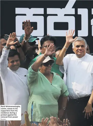  ??  ?? Ranil Wickremesi­nghe, centre, waves to his supporters from his residence during a protest against his removal from power