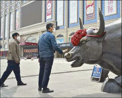  ?? AP ?? A man wearing a protective face mask touches the investment icon bull statue on display outside a retail and wholesale clothing mall in Beijing.