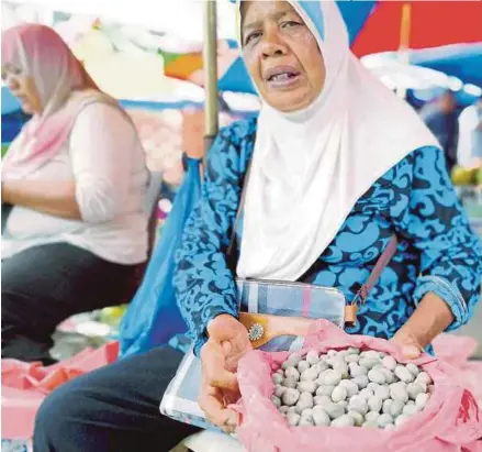  ?? [ FOTO POLIANA RONNIE SIDOM/BH ] ?? Faridah menunjukka­n buah 'komunggi' yang dijual di pasar tani di Sandakan.