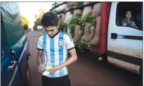  ?? ?? Wearing an Argentine soccer jersey, Fabian Acuna counts his weekly payment April 19 for harvesting yerba mate outside his home where the foreman drove to drop off his payment. Rich or poor, left or right, fan of Argentine soccer club Boca Juniors or its fierce rival River Plate, Argentines run on mate.