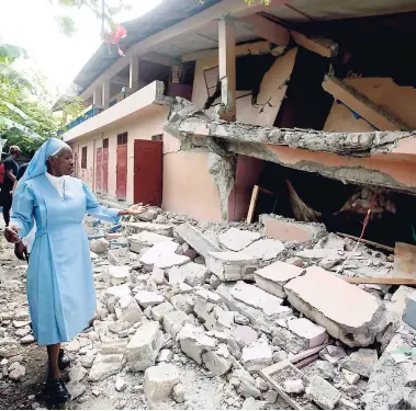  ?? AP ?? Maryse Alsaint walks alongside a school damaged by a magnitude 5.9 earthquake in Gros Morne, Haiti, last Sunday. Emergency teams worked to provide relief in Haiti on Sunday after the quake killed at least 15 people and left hundreds injured.