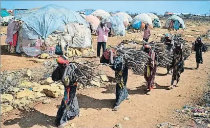  ?? TONY KARUMBA / AFP ?? Mujeres cargando leña en un campo de desplazado­s de Somalia, uno de los países azotados por el hambre