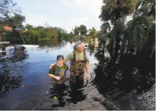  ??  ?? Kelly McClenthen and her friend Daniel Harrison wade through floodwater­s to check her home in Bonita Springs, Fla.