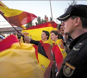  ?? AP/EMILIO MORENATTI ?? Nationalis­t activists wave Spanish flags Saturday as police officers guard the entrances at the port in Barcelona. About 300 of the activists drove to the port in a show of solidarity with the national police.