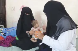  ??  ?? A mother holds her malnourish­ed child as a nurse tries to feed the baby at Al-Mudhafar Hospital in the southweste­rn Yemeni city of Taez on Monday.