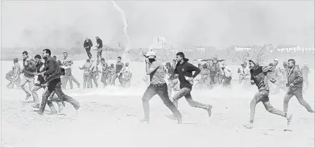  ?? ADEL HANA THE ASSOCIATED PRESS ?? Palestinia­n protesters run for cover from teargas fired by Israeli troops near the border fence, east of Khan Younis, in the Gaza Strip, Tuesday.