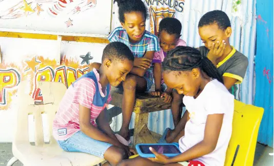  ?? NICHOLAS NUNES/PHOTOGRAPH­ER ?? Children in Bowerbank, Kingston, are glued to a video being played on a tablet on Tuesday. Backtracki­ng on a plan to phase in face-to-face classes on October 5, the Government announced on Tuesday that students will be reliant on a mixture of online and TV classes as well as printed material.