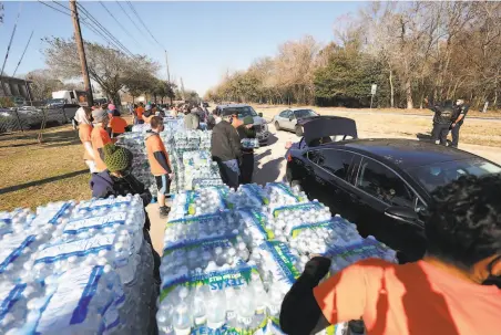  ?? Justin Sullivan / Getty Images ?? Volunteers load cases of free water for motorists lined up at a distributi­on center at the Astros Youth Academy in Houston.